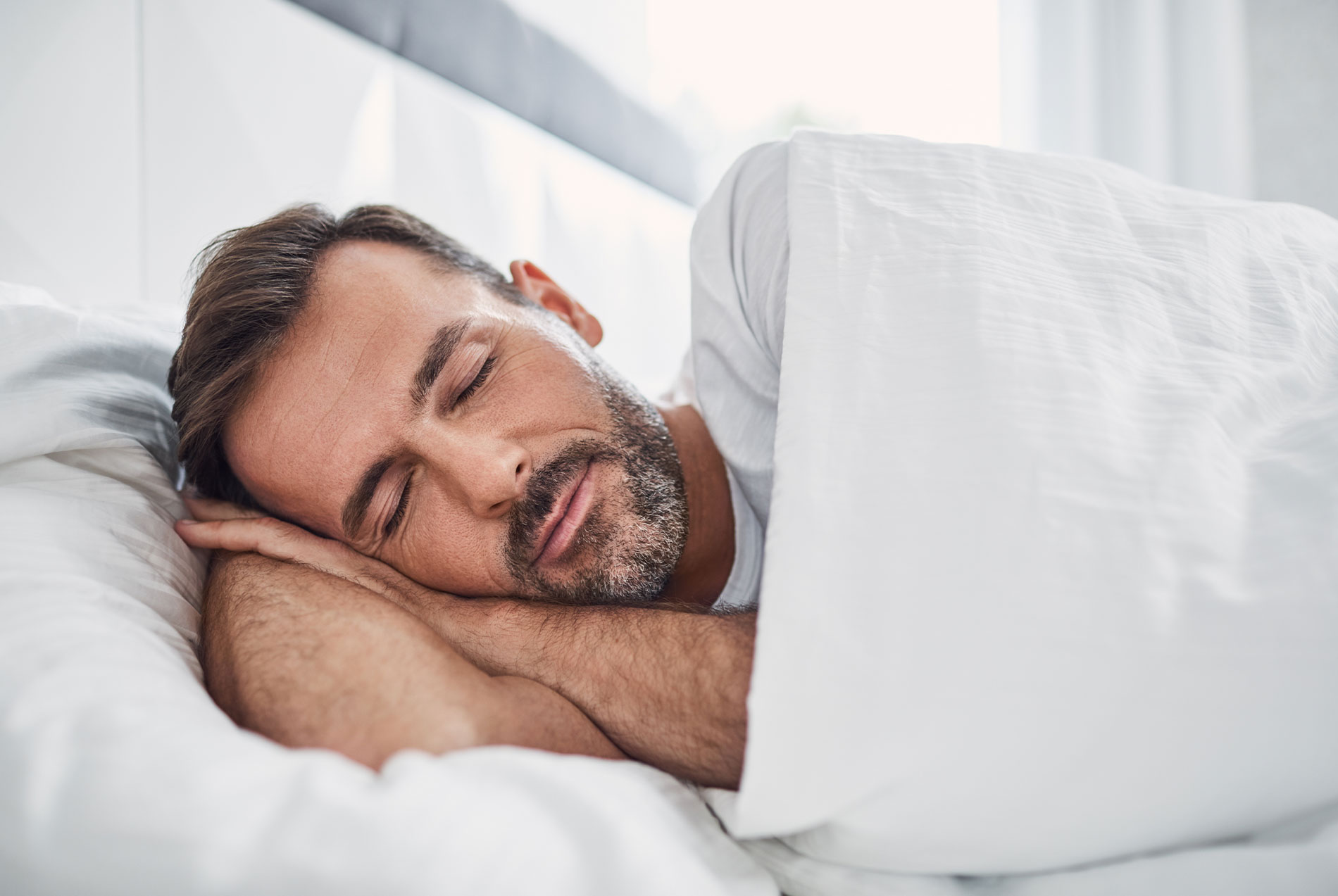 A man sleeping peacefully in bed with his eyes closed.